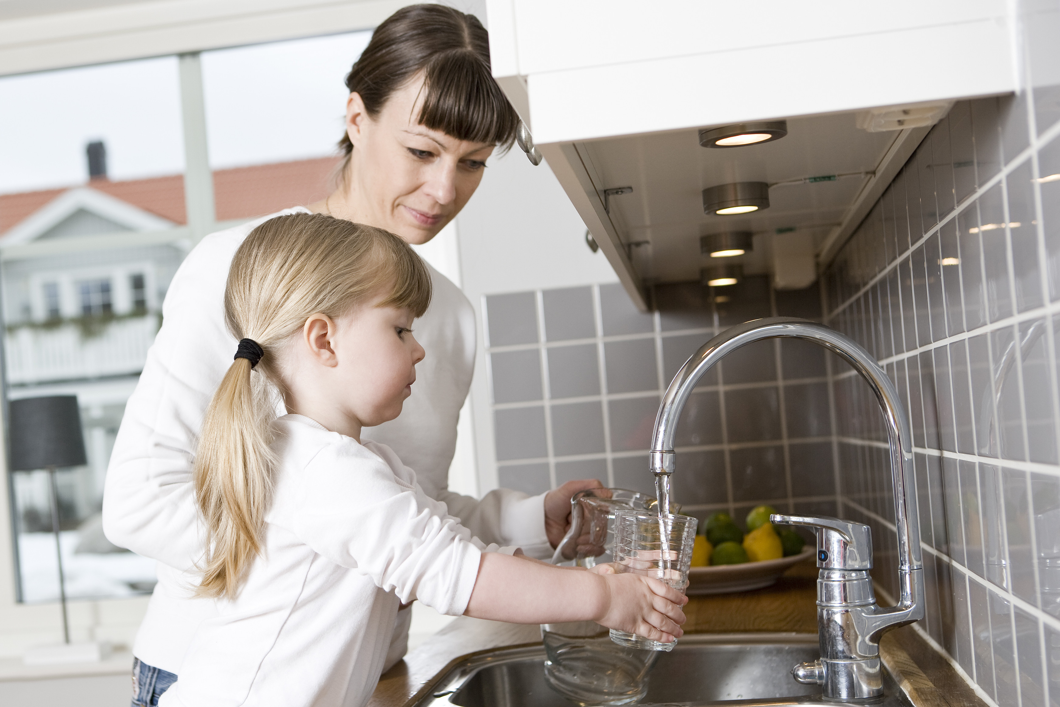 Mutter und Tochter füllen an der Spüle ihre Wassergläser auf